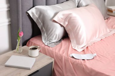 İçinde güzel ipek çarşaflar, uyku maskesi ve komodin olan bir yatak.