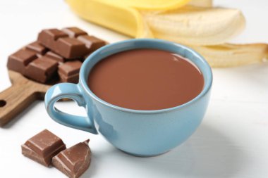 Lezzetli çikolatalı süt, parçalar ve muz beyaz ahşap masada, yakın plan.