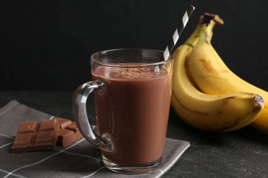 Cam bardakta lezzetli çikolatalı süt, siyah masada parçalar ve muzlar, yakın plan.