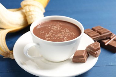 Lezzetli çikolatalı süt, parçalar ve muz mavi ahşap masada, yakın plan.