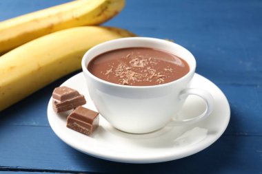 Lezzetli çikolatalı süt, parçalar ve muzlar mavi ahşap masada, yakın plan