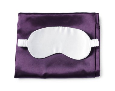 Beyaz arka planda ipek çarşaflar ve uyku maskesi, üst manzara.