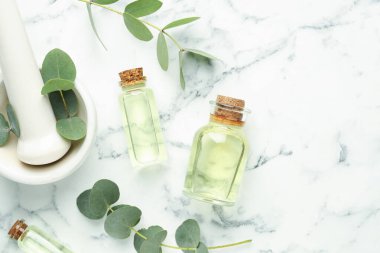 Önemli yağ şişeleri, okaliptüs yaprakları, beyaz mermer masa üzerinde havan ve tokmak, düz zemin. Metin için boşluk