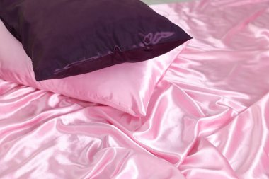 Lüks pembe ipek çarşaflar ve yastıklar yatakta, yakın plan.
