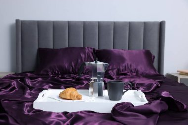 Mor ipek çarşaflar, içinde kahve ve kruvasan olan tepsi.