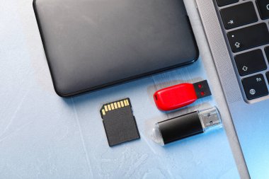Flaş bellek, hafıza kartı, harici hard disk ve dizüstü bilgisayar açık gri tabloda, düz konum