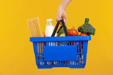 Sarı arka planda farklı ürünleri olan alışveriş sepeti tutan adam, yakın plan.