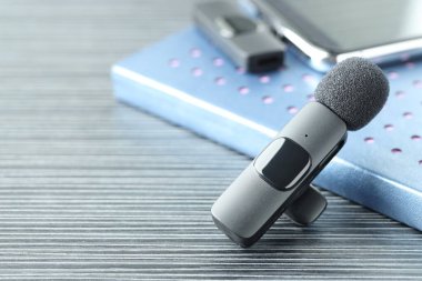 Lavalier mikrofon, kablosuz alıcısı olan akıllı telefon ve siyah ahşap masadaki defter, yakın plan.