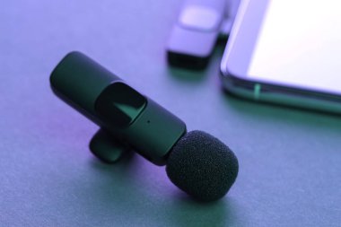 Lavalier mikrofon ve kablosuz alıcısı olan akıllı telefon karanlık masada neon ışıklarda, yakın plan.
