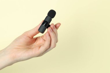 Bej arka planda lavalier mikrofon tutan kadın, yakın plan. Metin için boşluk