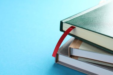 Kırmızı kurdele yer imi ve açık mavi arka planda renkli kitap, yakın plan. Metin için boşluk
