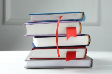 Gri duvara karşı beyaz tahta masada kırmızı kurdele yer imleri olan kitaplar, yakın plan.