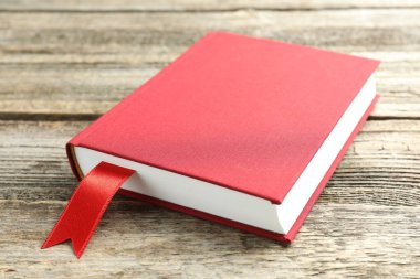 Ahşap masada kırmızı kurdele yer imi olan bir kitap, yakın plan.