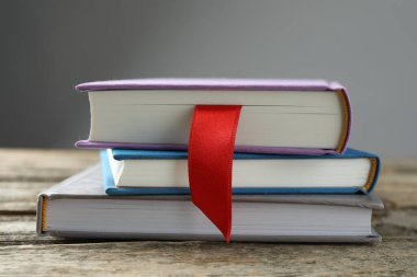Kırmızı kurdele yer imi ve ahşap masadaki renkli kitap gri arkaplanda, yakın plan