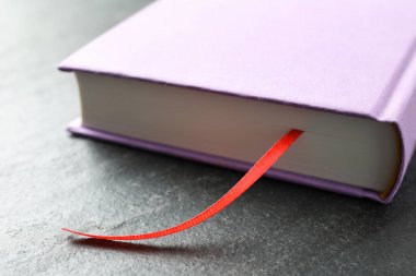 Koyu desenli masa üzerinde kırmızı kurdele yer imi olan kitap, yakın plan.