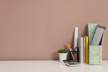 Beyaz ofis masasındaki farklı kırtasiye, çiçek dekoru ve hesap makinesi koyu bej arkaplan, metin için boşluk