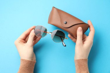 Güneş gözlüklü ve açık mavi arka planda çantası olan bir kadın.