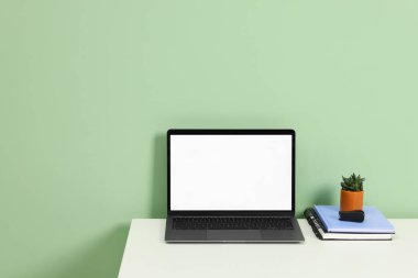 Modern dizüstü bilgisayarı açık yeşil duvarın yanındaki beyaz masada olan şık bir iş yeri. Metin için boşluk