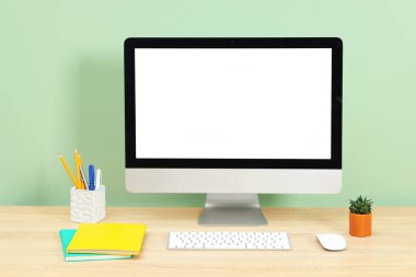 Modern bilgisayarlı şık bir iş yeri açık yeşil duvarın yanındaki ahşap masada.