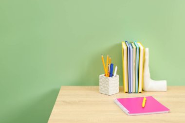 Açık yeşil duvarın yanındaki ahşap masasında kırtasiye malzemesi olan şık bir iş yeri. Metin için boşluk