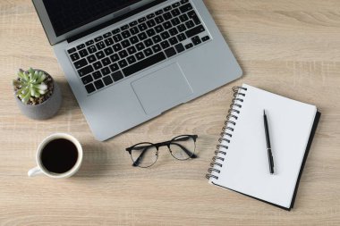 Ofis malzemeleri, dizüstü bilgisayar ve bir fincan kahveyle ahşap masada düz konumda duruyordu.