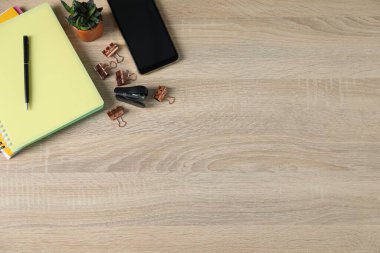 Ofis malzemeleri, akıllı telefon ve ev bitkisiyle ahşap masa üzerinde düz bir kompozisyon. Metin için boşluk