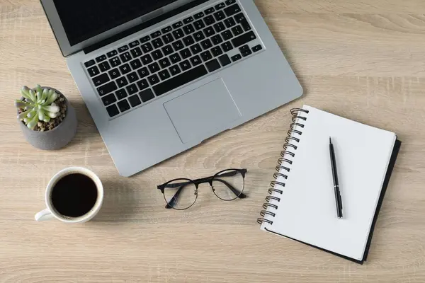 Ofis malzemeleri, dizüstü bilgisayar ve bir fincan kahveyle ahşap masada düz konumda duruyordu.