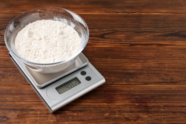 Elektronik mutfak terazisi ve ahşap masa üzerinde bir kase un. Metin için boşluk