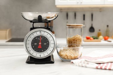 Retro mekanik mutfak terazisi ve beyaz mermer masa üzerinde çiğ makarna.