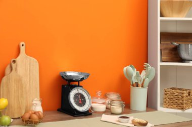 Kitchen scale, products and cooking utensils on wooden table. Space for text