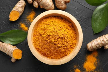 Kasede akromatik zerdeçal tozu, taze kökler ve siyah masa üzerindeki yapraklar, düz uzanmış.