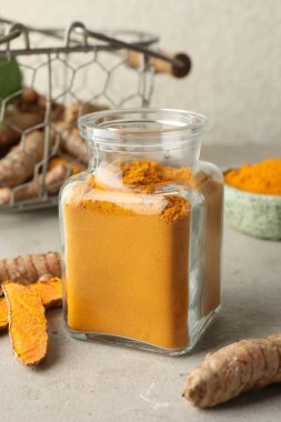 Cam kavanozda Aromatik zerdeçal tozu ve açık gri masada taze kökler.