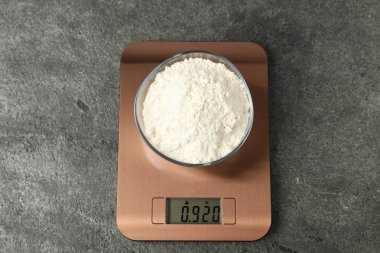 Modern elektronik mutfak terazisi, gri masa üzerinde bir kase un, üst manzara.