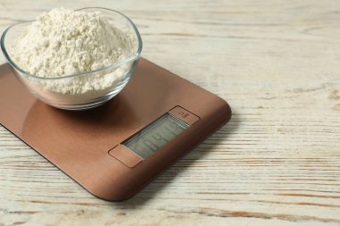 Modern electronic kitchen scale with bowl of flour on wooden table, closeup. Space for text