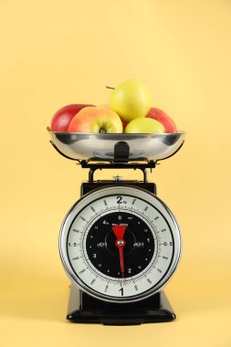 Mechanical kitchen scale with bowl of apples on yellow background