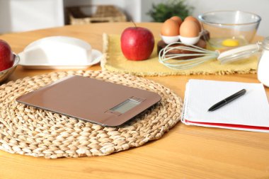 Elektronik mutfak ölçeği, ürünler ve ahşap masa üzerindeki kırtasiye.