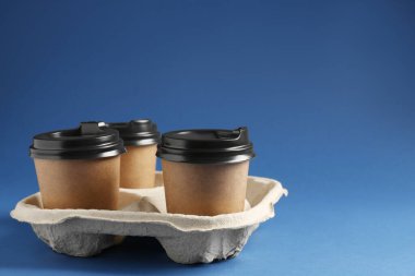 Kağıt kahve bardakları mavi arka planda karton tutacakta. Metin için boşluk