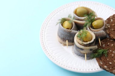 Zeytinli lezzetli ringa dürümleri, açık mavi arka planda dereotu ve ekmek, yakın plan. Metin için boşluk