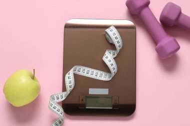 Elektronik mutfak terazisi, mezura, pembe zemin üzerinde dambıl ve elma, düz zemin. Diyet