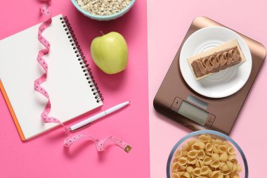 Elektronik mutfak ölçeği, mezura, not defteri ve pembe arka plandaki ürünler, düz konum. Kalori kontrolü