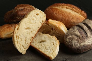 Siyah arkaplana karşı koyu dokulu masadaki farklı taze ekmek türleri, yakın plan