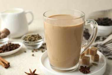 Cam bardakta Aromatik Masala çayı, beyaz desenli masada baharatlar ve kahverengi şeker, yakın plan.