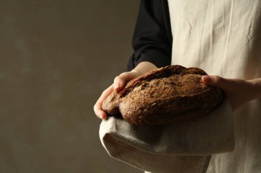 Gri arka planda taze ekmek somunu olan kadın, yakın plan.