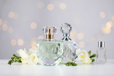 Aromatik parfüm şişeleri ve çiçekler, arka plandaki gri ışıklara karşı, yakın plan. Bokeh etkisi