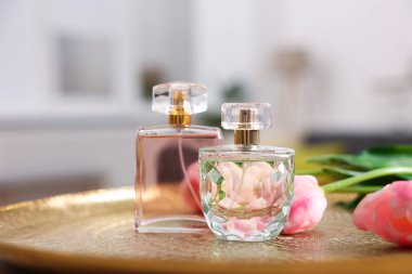 Aromatik parfüm şişeleri ve çiçekleri bulanık arka plana karşı desenli tabakta, yakın plan