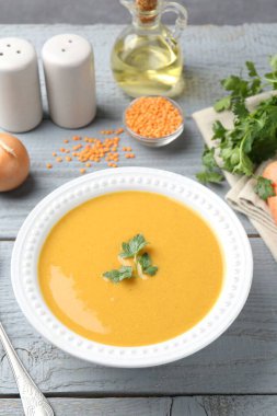 Gri ahşap masada servis edilen lezzetli mercimek kremalı çorba, yakın plan.