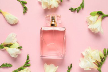 Bir şişe parfüm ve pembe arka planda güzel çiçekler.