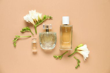 Düz kompozisyonda aromatik parfüm şişeleri ve bej arka planda güzel çiçekler vardı.