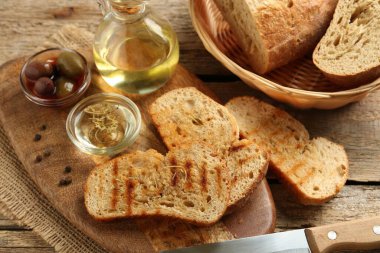Ahşap masada yağlı, zeytinli ve baharatlı tost ekmeği yakın plan.