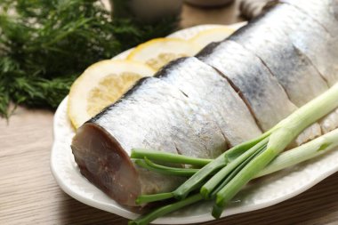 Limon dilimli lezzetli ringa balıkları, yeşil soğan ve ahşap masada dereotu, yakın plan.